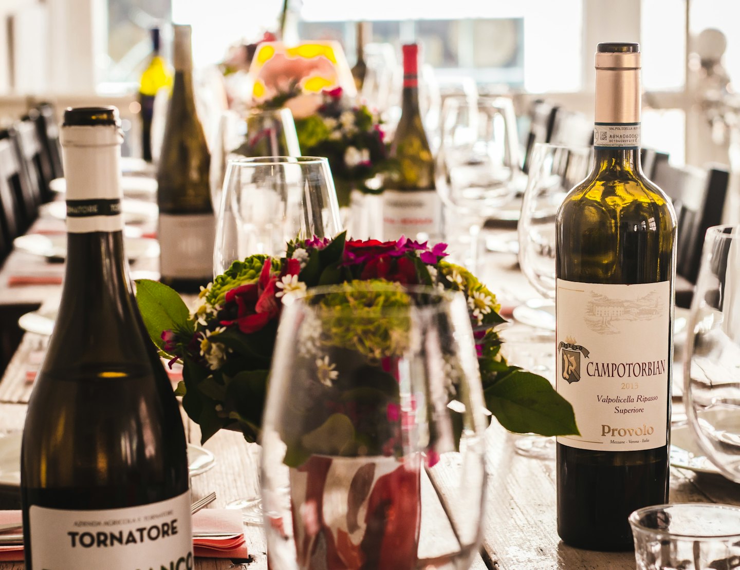 Elegant wine bottles and glasses arranged on a rustic table with floral centerpieces.