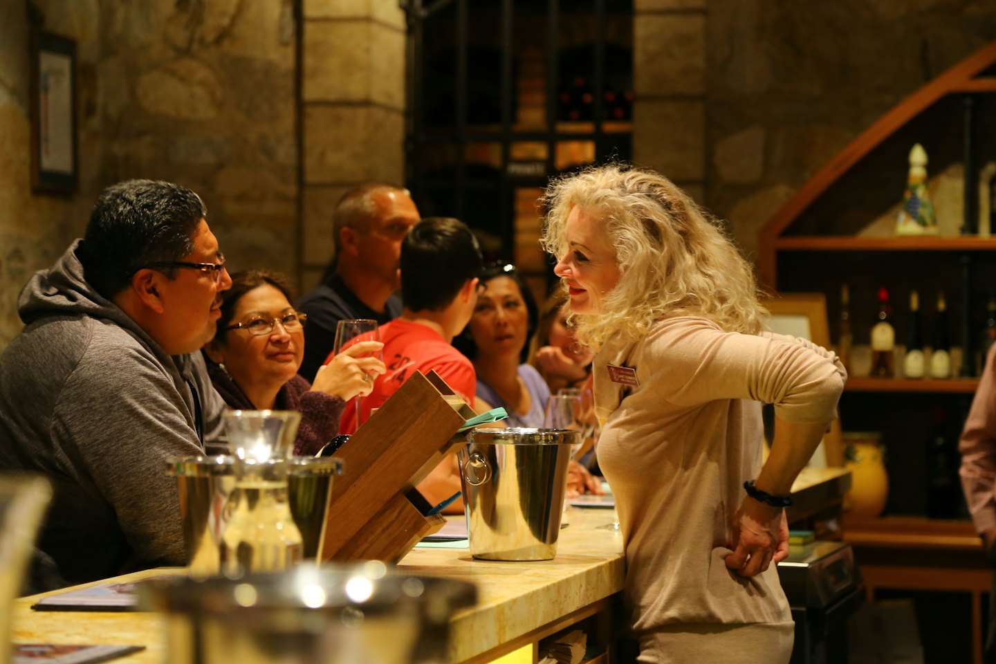 A woman gestures to customers during a wine tasting event.