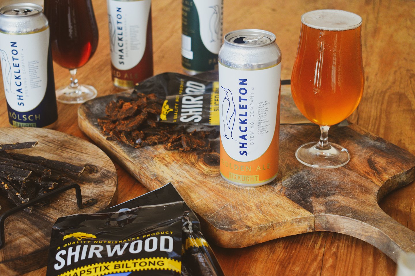 Shackleton Brewing Company beer cans and Shirwood meat snacks on a wooden table.